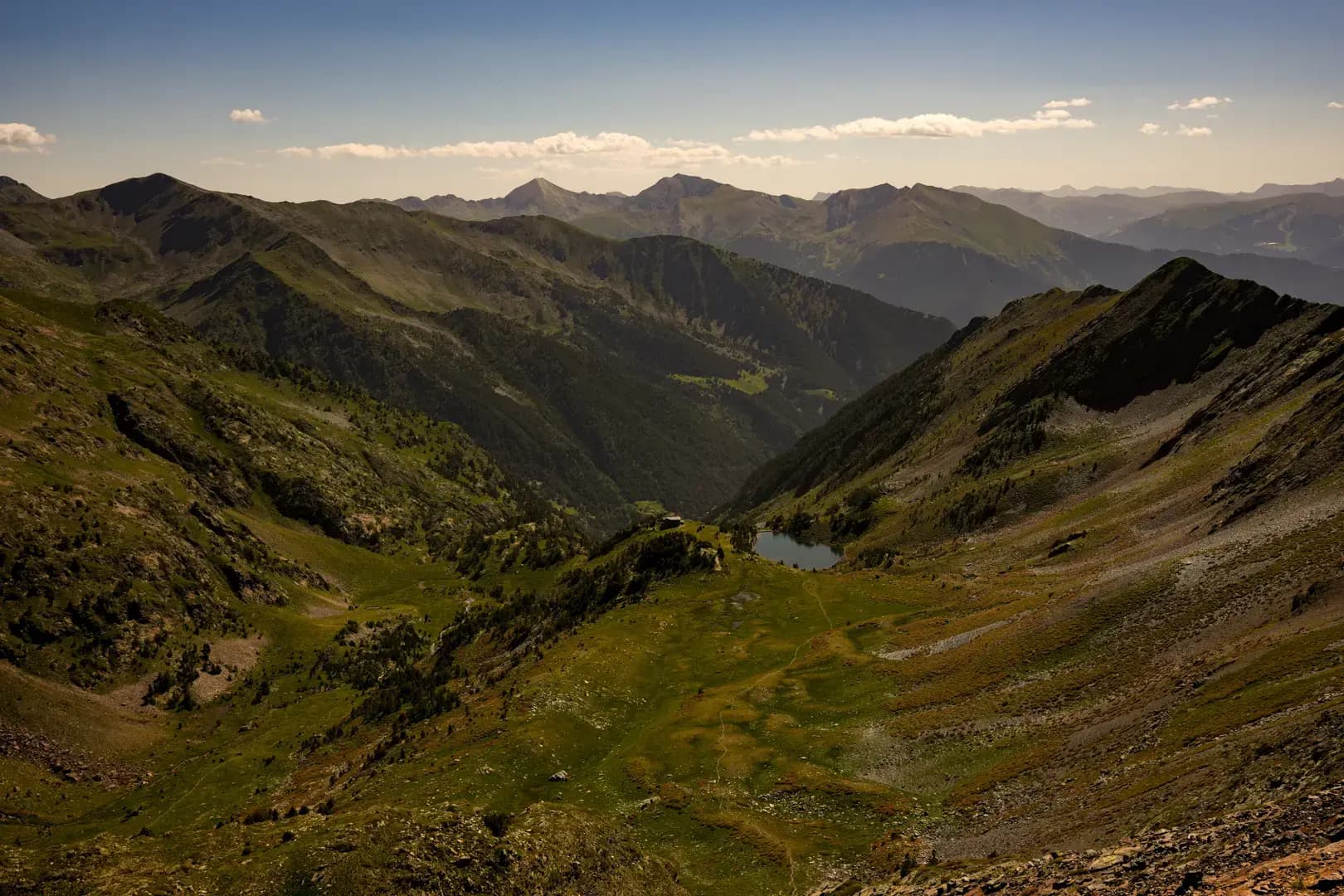 Vall de muntanya andorrana amb un llac al fons, sota la llum de la tarda.