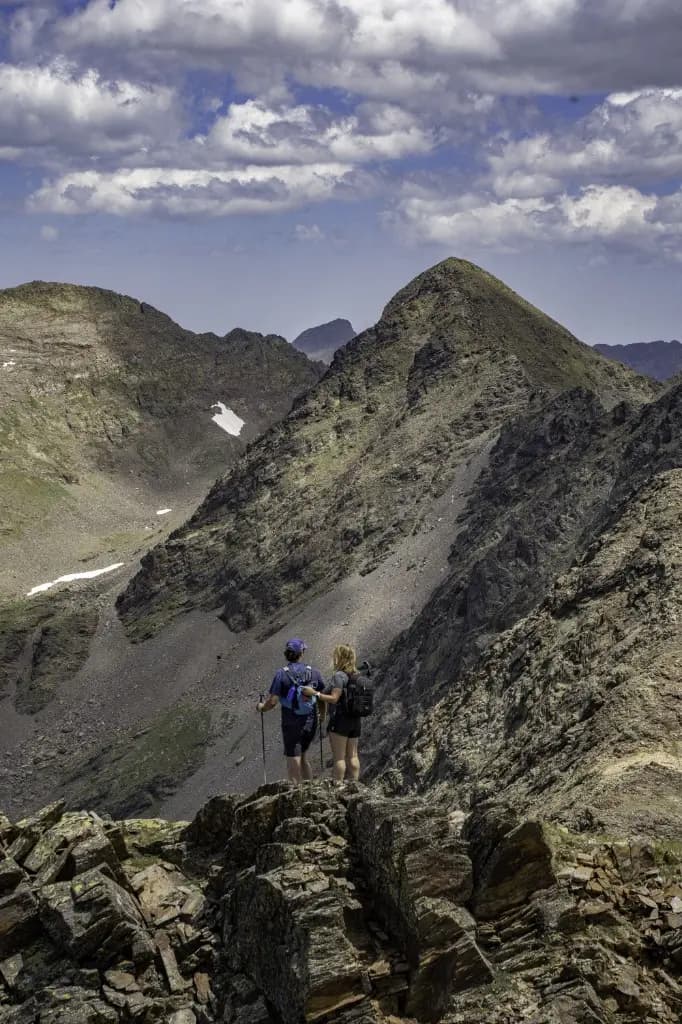 Dos excursionistes pujant per un vessant rocós sota un cim dels Pirineus andorrans.